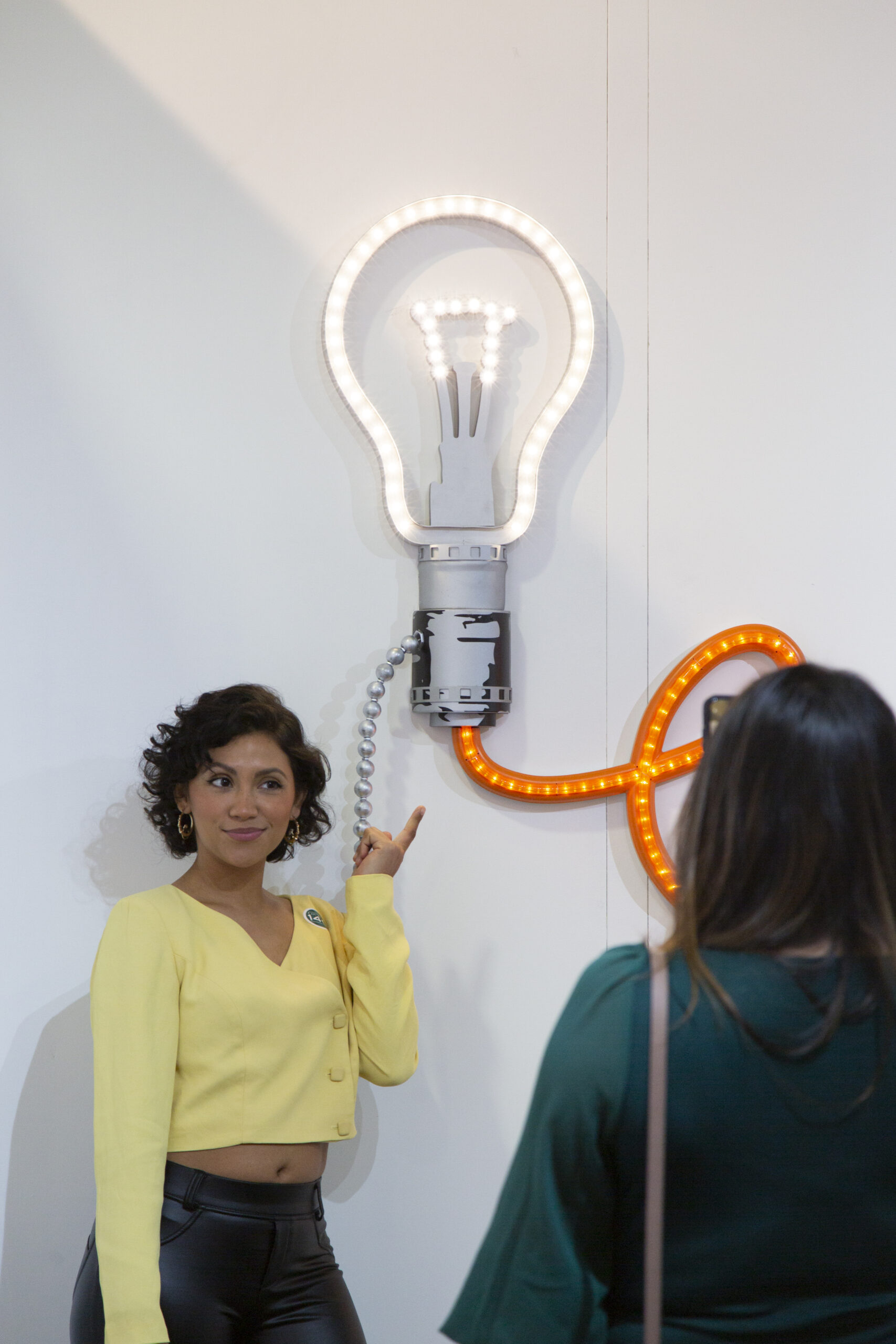 young woman points at an artwork of a light bulb