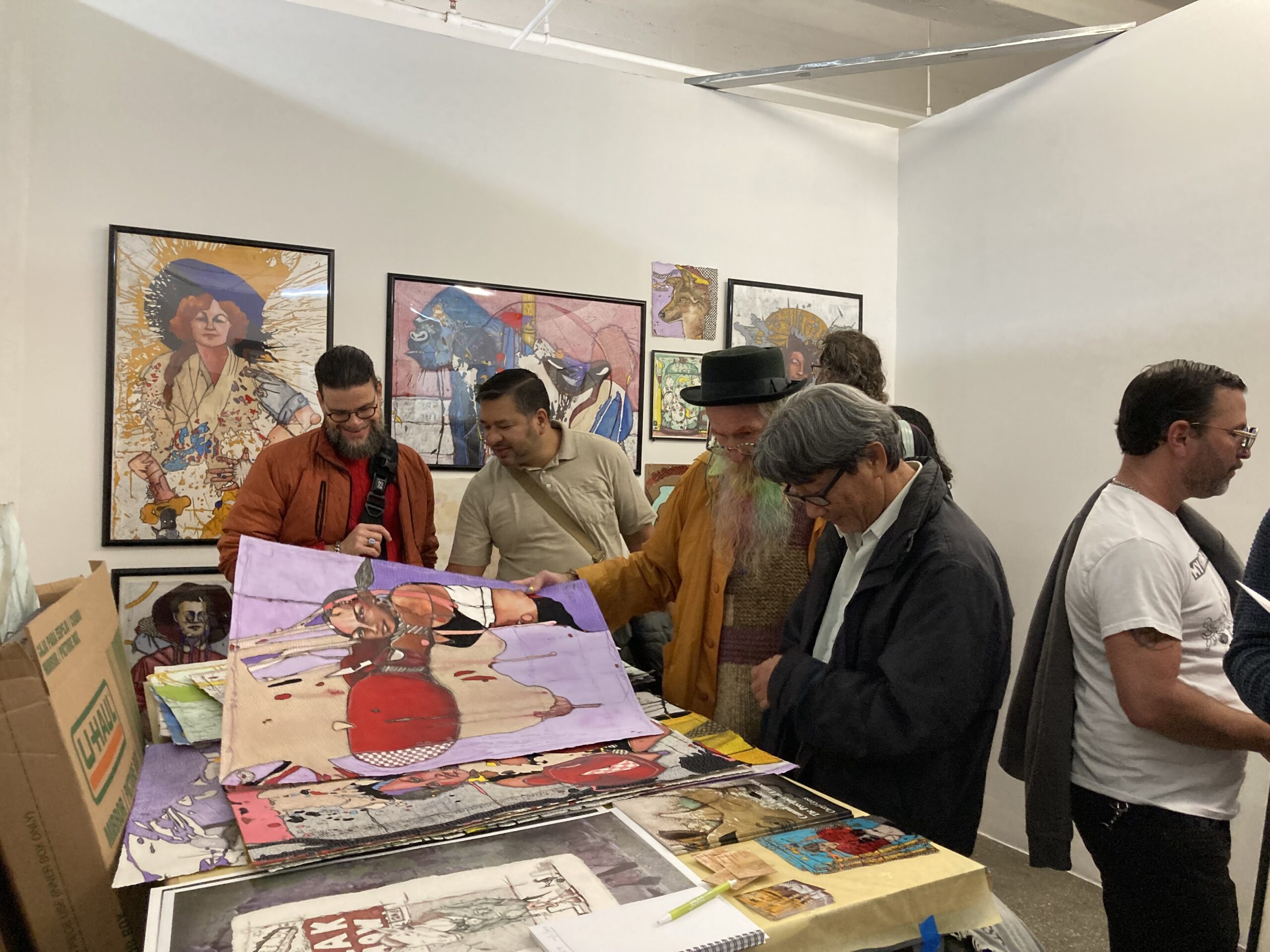 artist Debasish Sinha discusses his artwork with a visitor in his studio with small still life and landscape paintings on the wall in the background